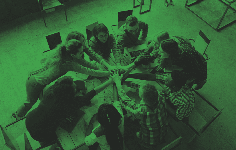 grupo de pessoas juntando as mãos ao centro de uma mesa