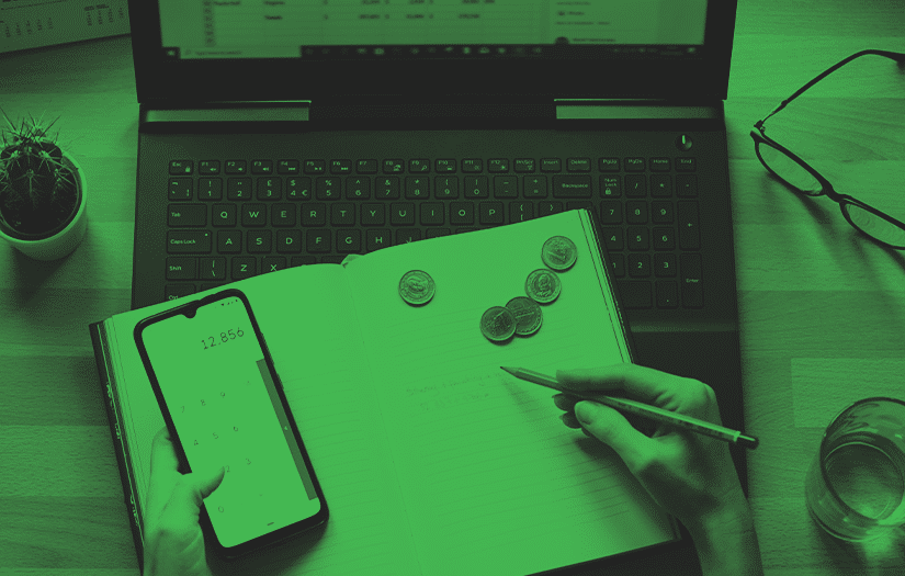Uma pessoa fazendo contas com algumas moedas na calculadora de celular, em cima de um caderno algumas moedas