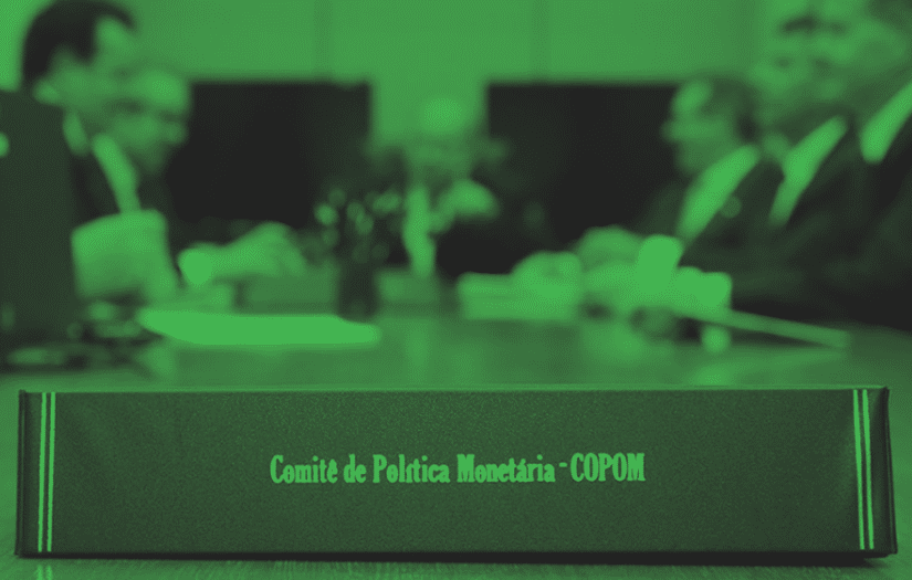 Uma mesa de executivos com uma placa sobre a mesa onde está escrito "Comitê de Política Monetária - COPOM"